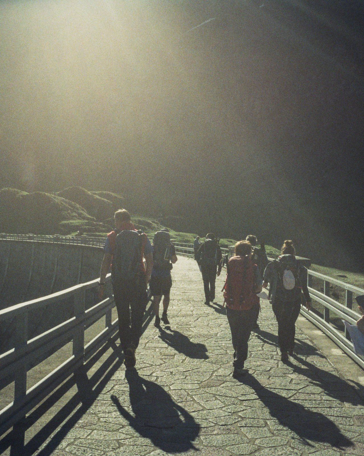 Escursionisti in controluce sul camminamento di una diga, con le ombre lunghe