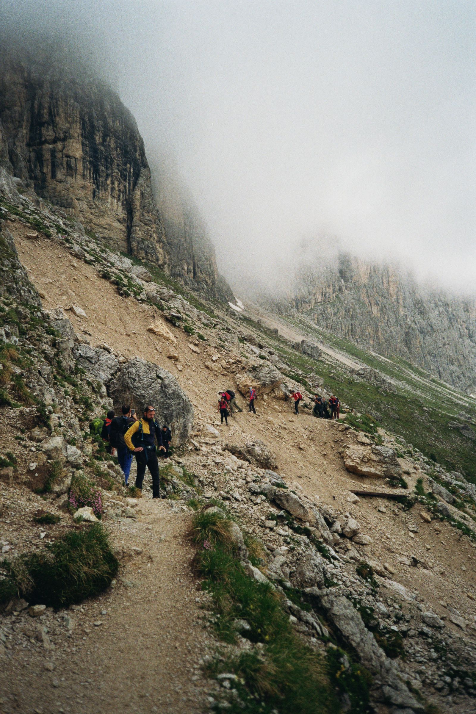 Un escursionista su un sentiero di sassi che sale verso pareti di roccia avvolte dalla nebbia